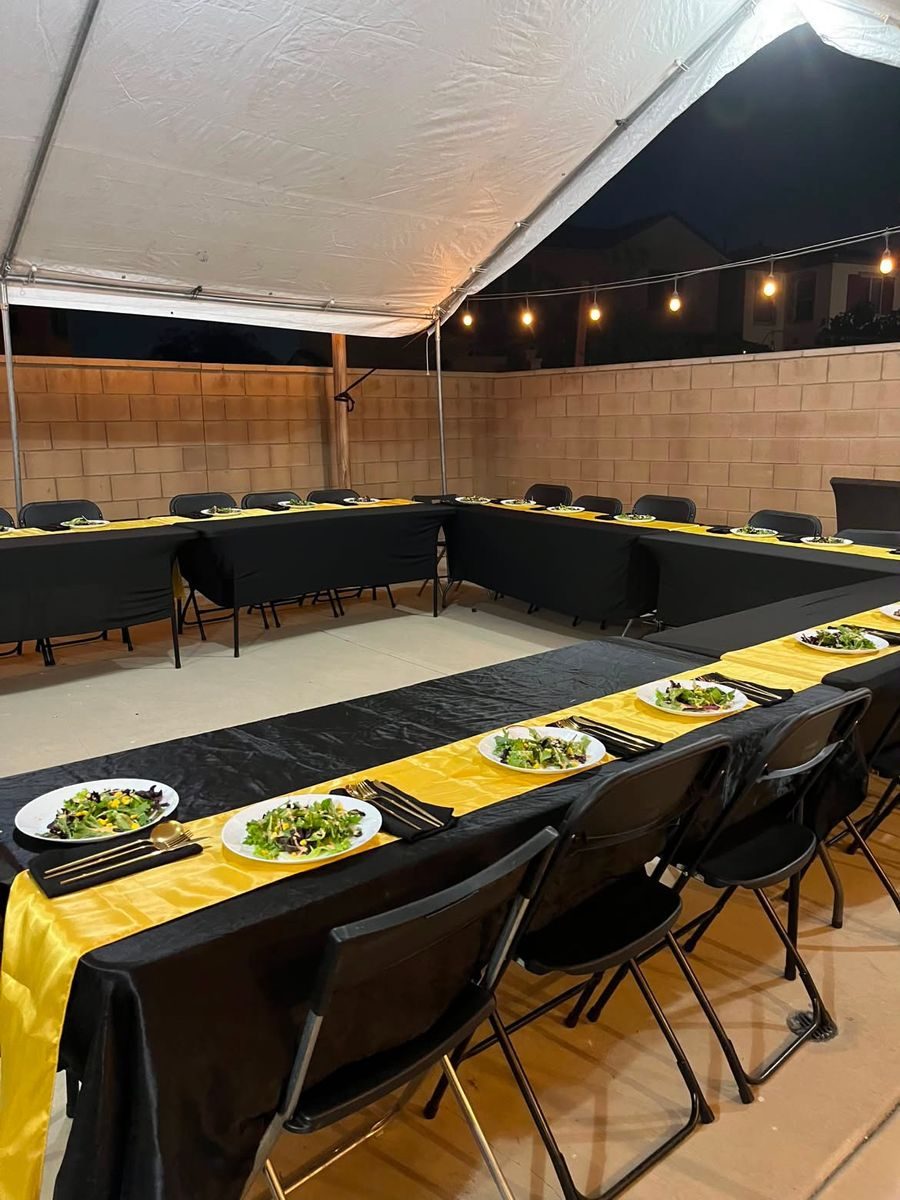 Long table set in black and gold under a tent before a hibachi dinner