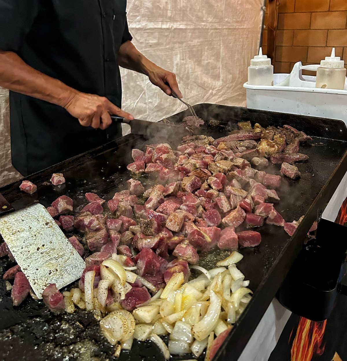 Chef searing grass-fed beef and onions on the flat-top griddle at a private event